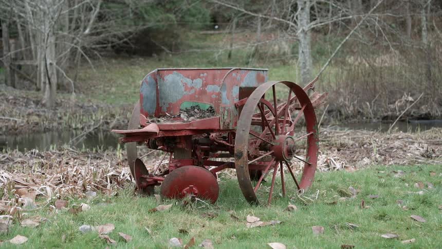 An old plow is sitting idle near a pond in a rural area during the day