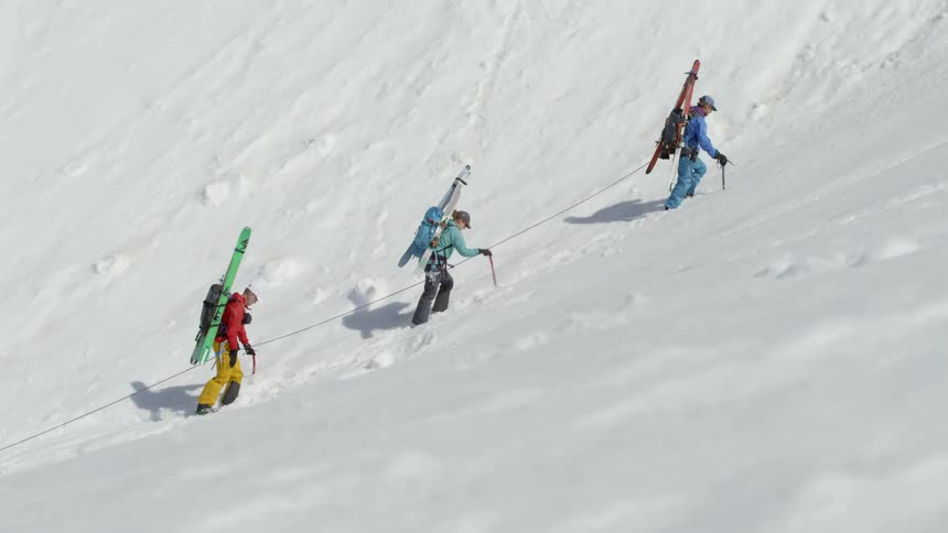 Four people use a rope and sticks up climb up a snowy mountain
