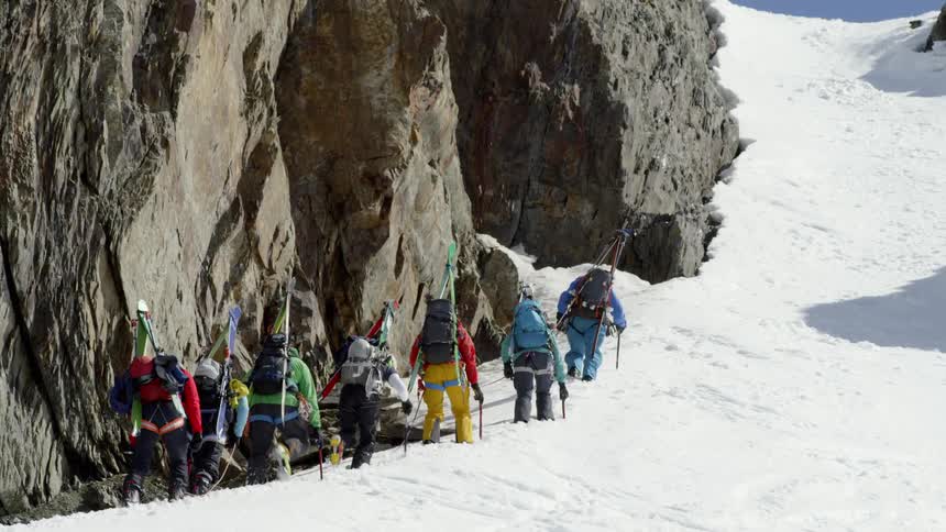 The people climb up the steep slope of the mountain together on rope