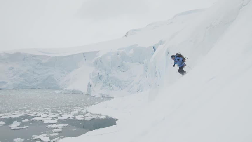 Man wears a backpack as he skis down a snowy mountain