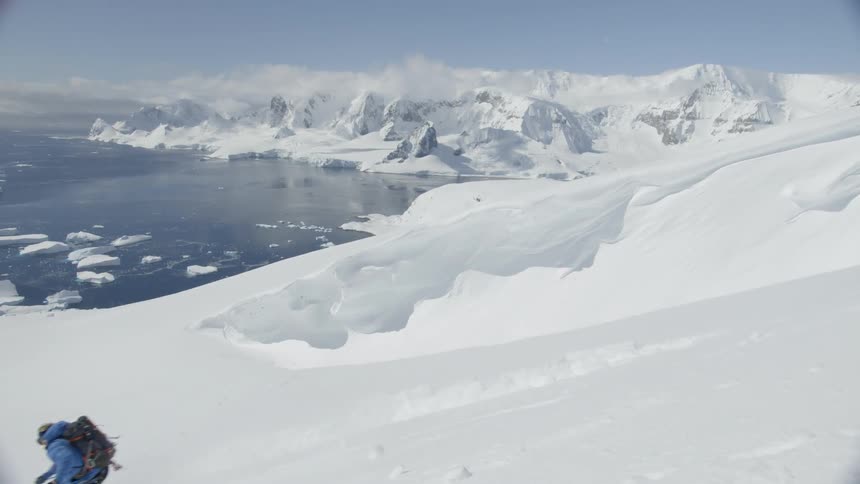 Person skis down a steep hill near an icy lake
