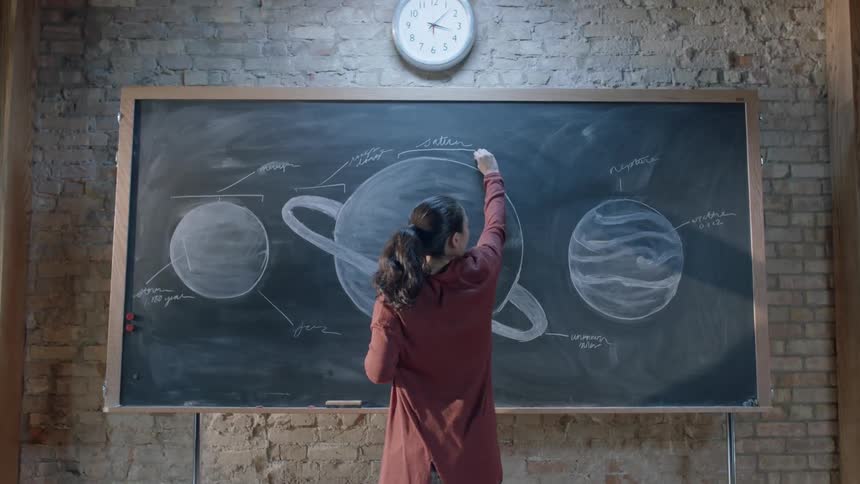 A teacher draws planets on a chalkboard