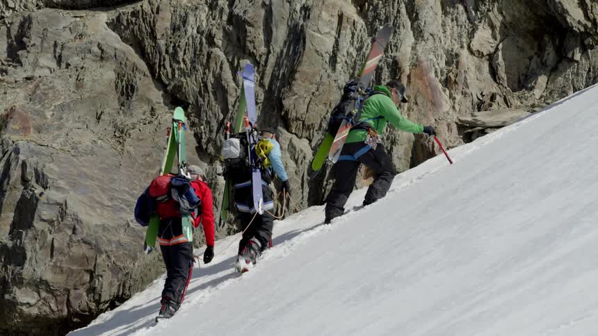 Group of people use sticks and a rope to hike up a snowy mountain