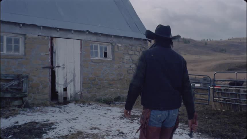 A cowboy walks towards the barn