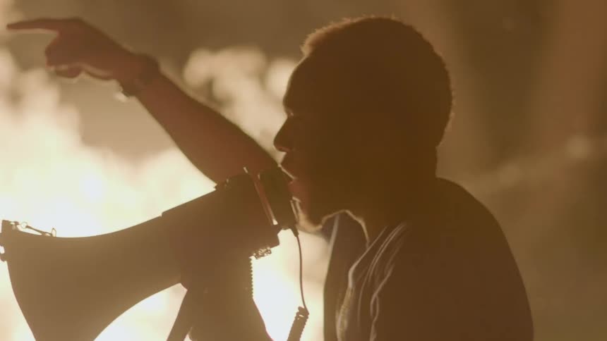 Person yells into a megaphone near a blazing fire