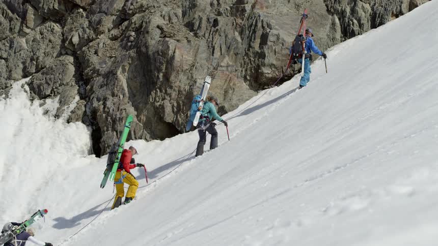 Four people use a rope and ice axes to climb up a snowy mountain