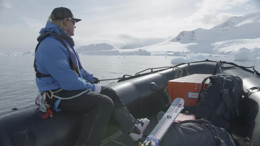 A man rides in a boat near snowy mountains