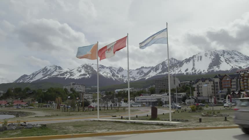 Three flags blow in the wind near a building and snowy mountains