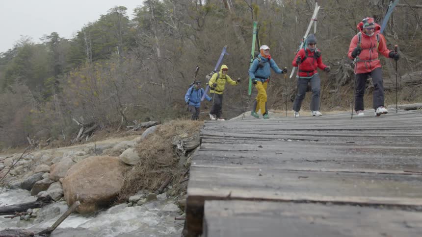 Group of skiers hike towards wooden bridge by a bubbling stream