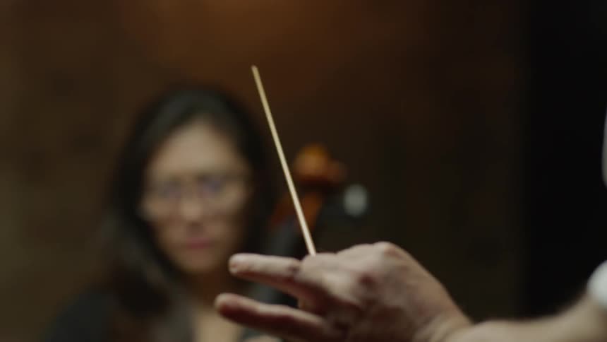 A conductor waves a wand near a cellist
