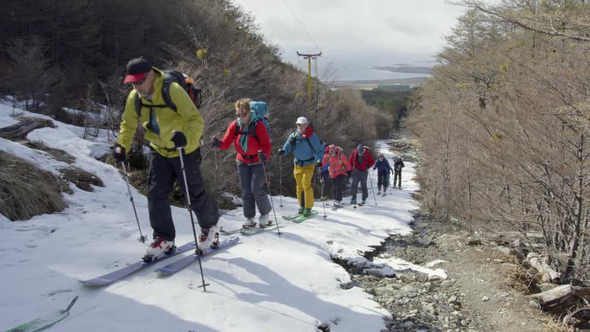 A group of men and women on skis push themselves up a hill with their poles