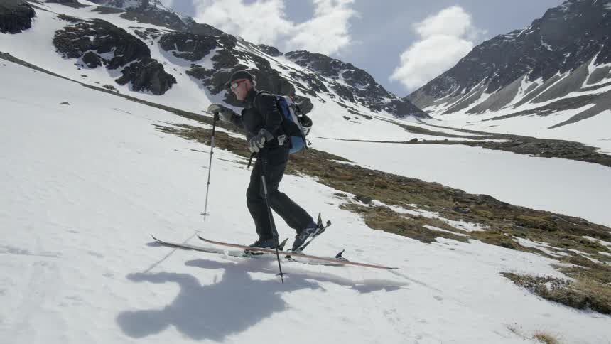Man on skis pushes himself up a snowy mountain with his poles
