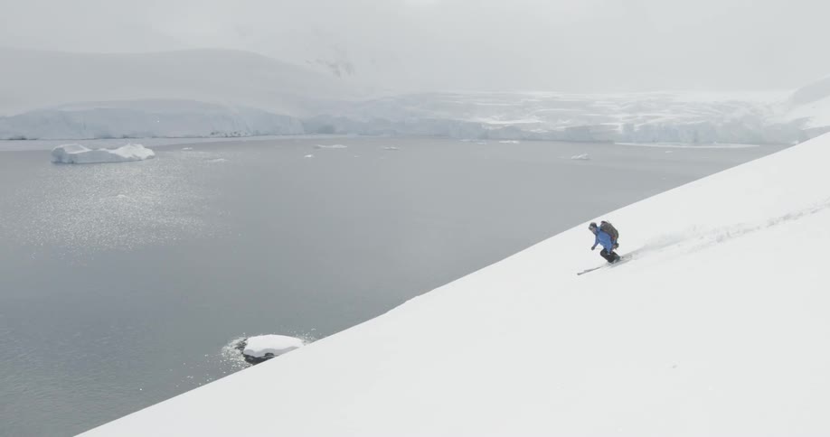 The person is skiing fast down the slope towards the water