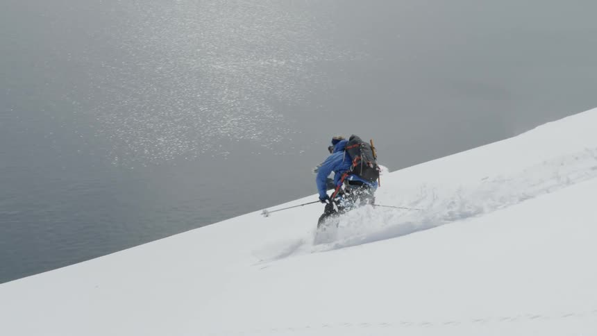 A person skiing down a large slope near a big body of water