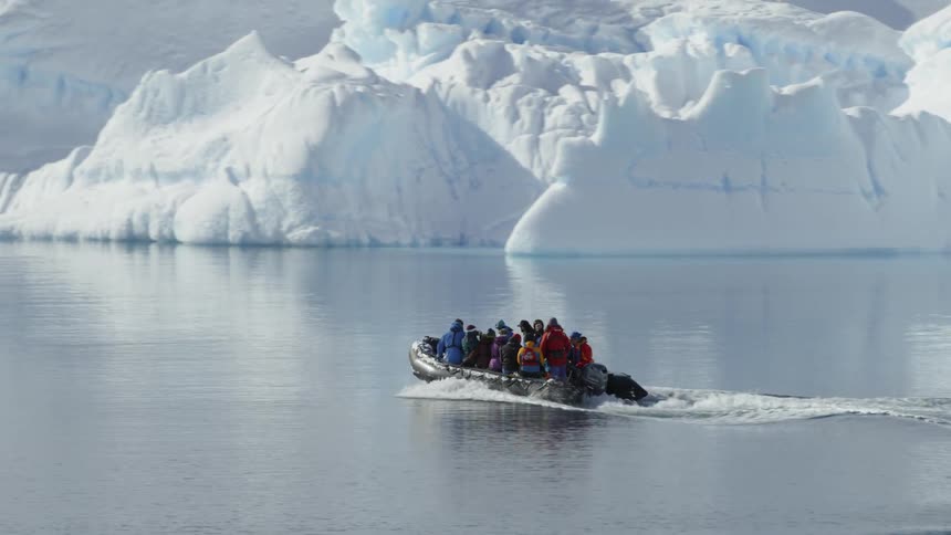 A full boat of people travels over the calm waters in front of iceberg