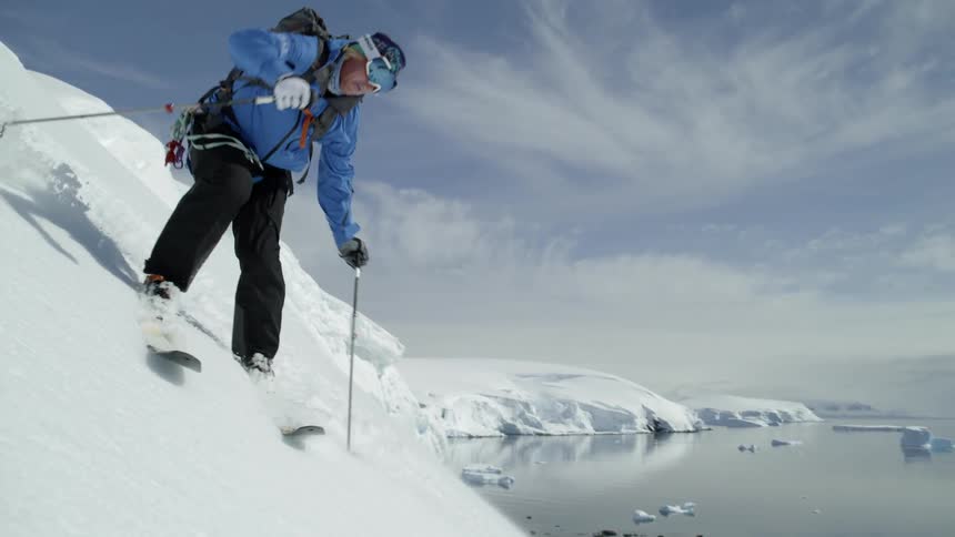 Man skis down a snowy mountain near a lake