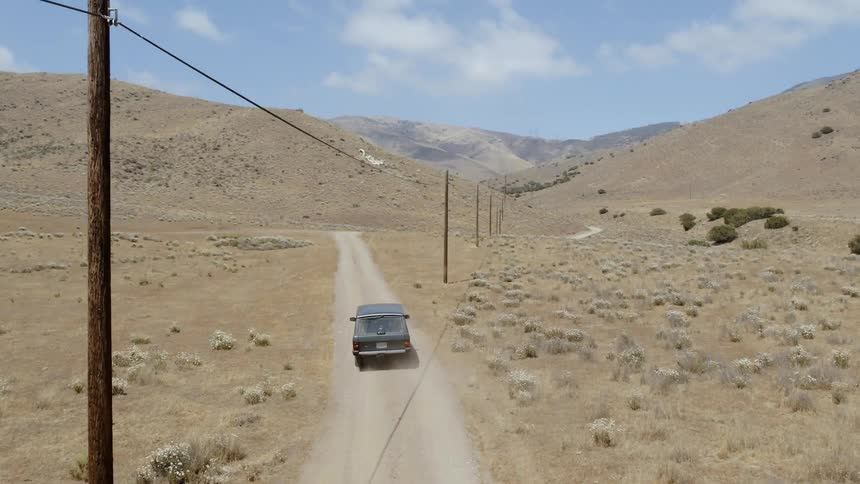 Vehicle travels down a dirt road under a blue sky