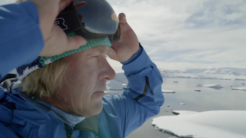 A man puts on ski goggles in snowy mountains