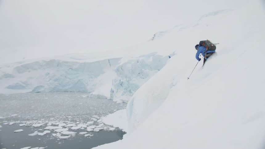 Skier going down a snowy hill next to a frozen lake