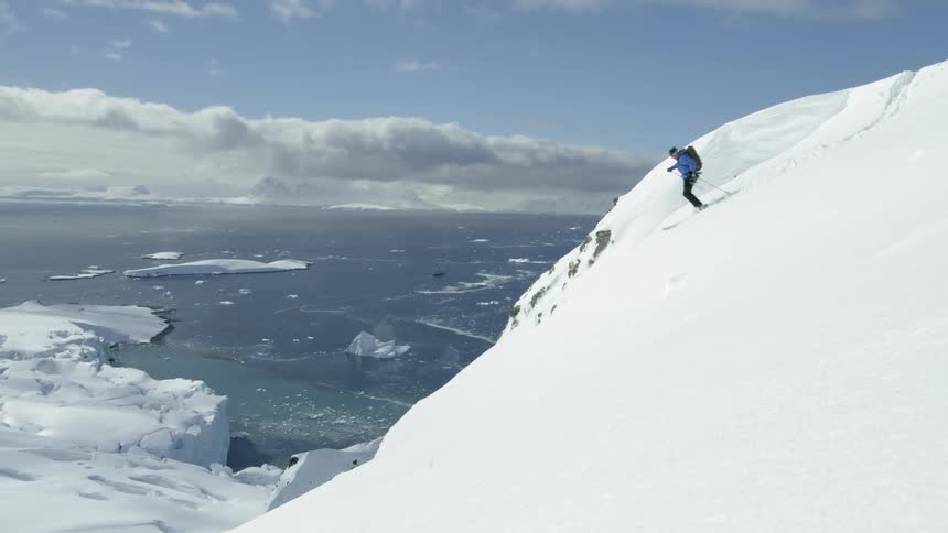 Person snows down a steep snowy mountain near a large lake