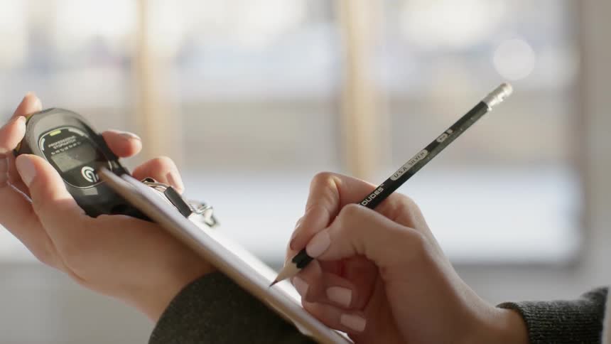 A person is writing on a clipboard with a pencil