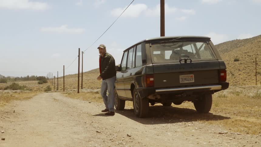 Vehicle comes to a stop on a dirt road and the driver appears to be angry as he walks around to complain on the other side on a cloudy day