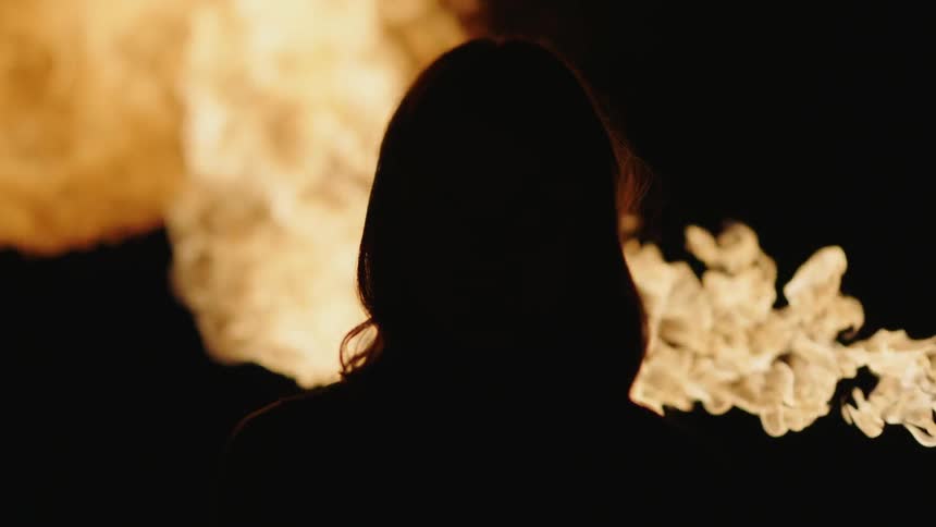 Woman standing as a ball of fire blows up in the dark background