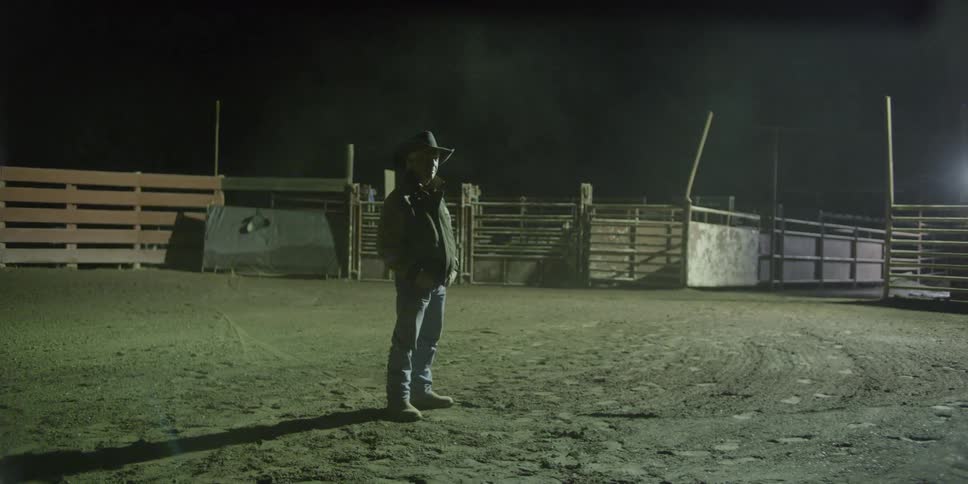 A cowboy stands in the rodeo rink at night