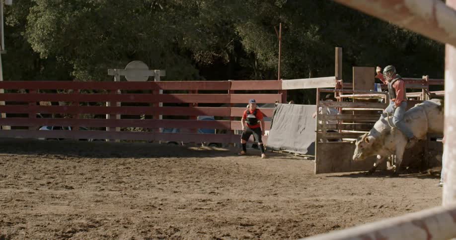 A cowboy is pulling a gate open so a cowboy on a bull can start his ride