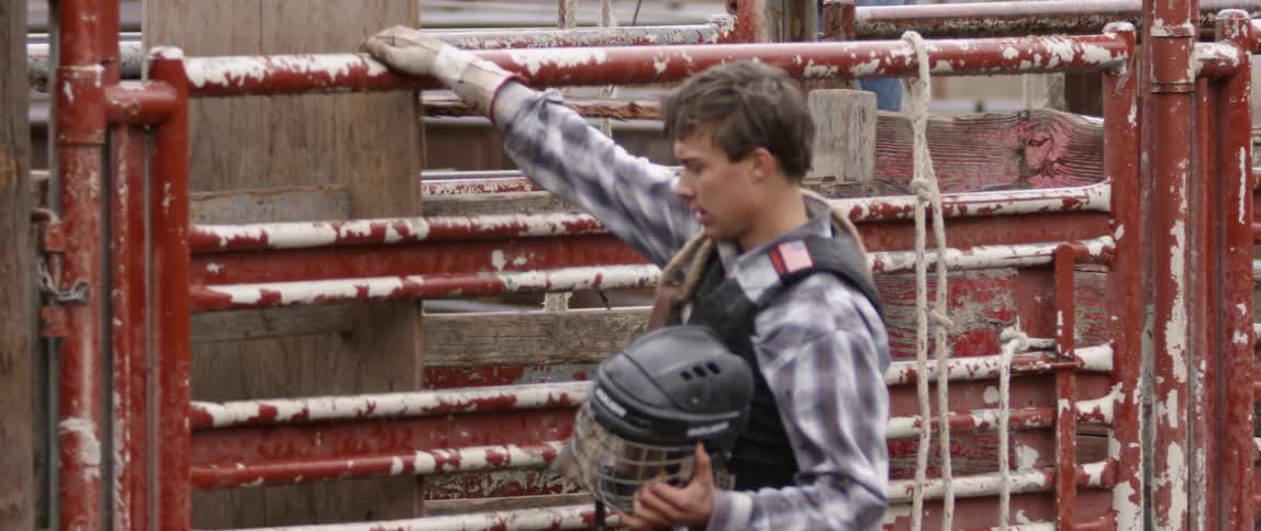 A bull rider climbs a fence