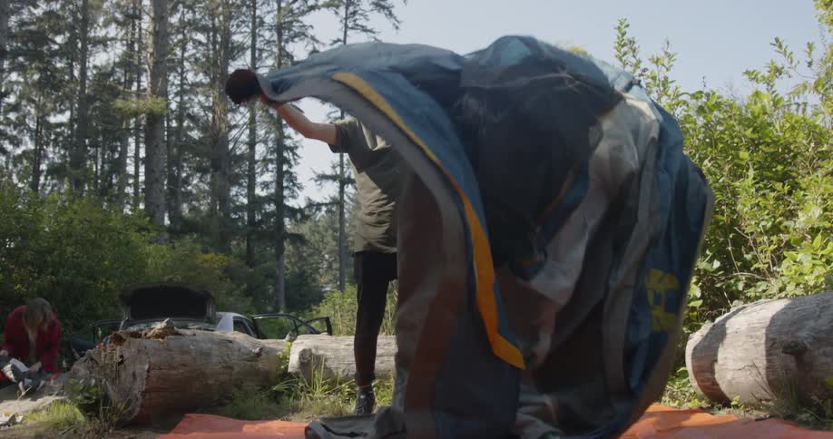 A man lays out a tent on a sunny day
