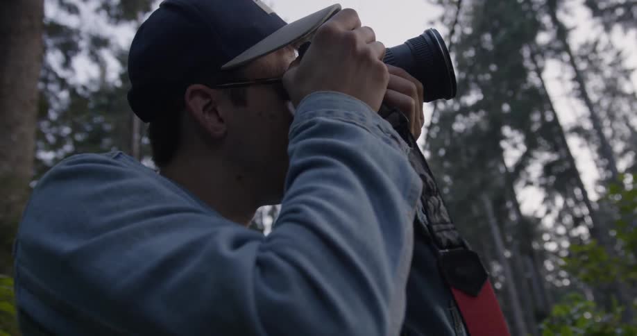 Man wearing glasses takes a picture in the forest