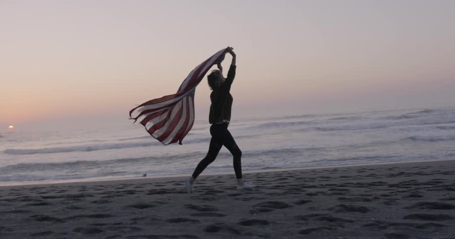 A woman runs on the beach with a flag at sunset