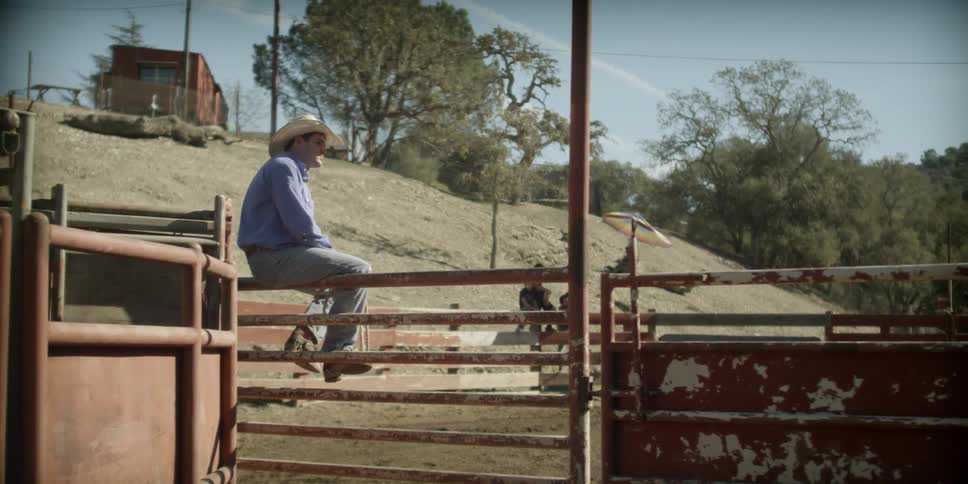 A cowboy sits on top of a fence