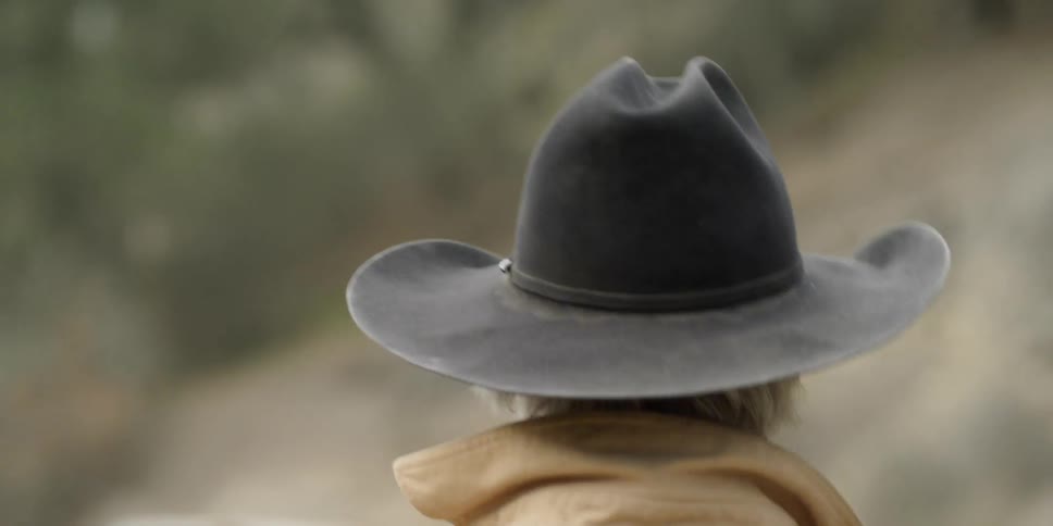 A man wearing a cowboy hat is walking outside during the day