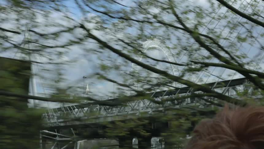 A car drives under a city bridge with a ferris wheel behind it