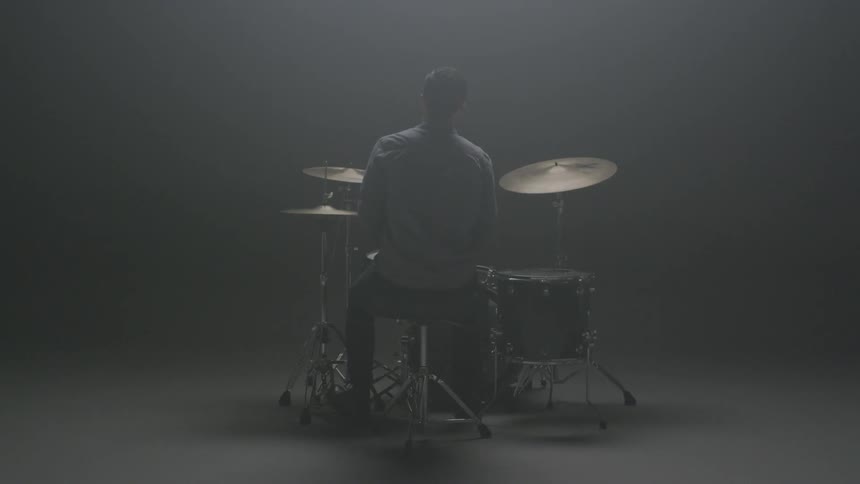 A man plays drums in a dim room