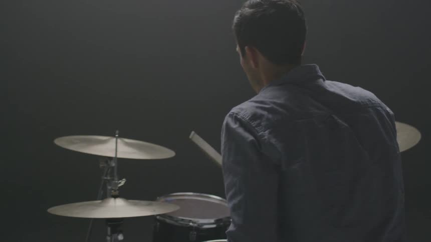 A man plays drums in a dim room