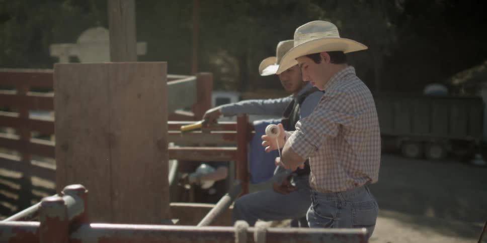 Cowboys stand near a fence on a ranch