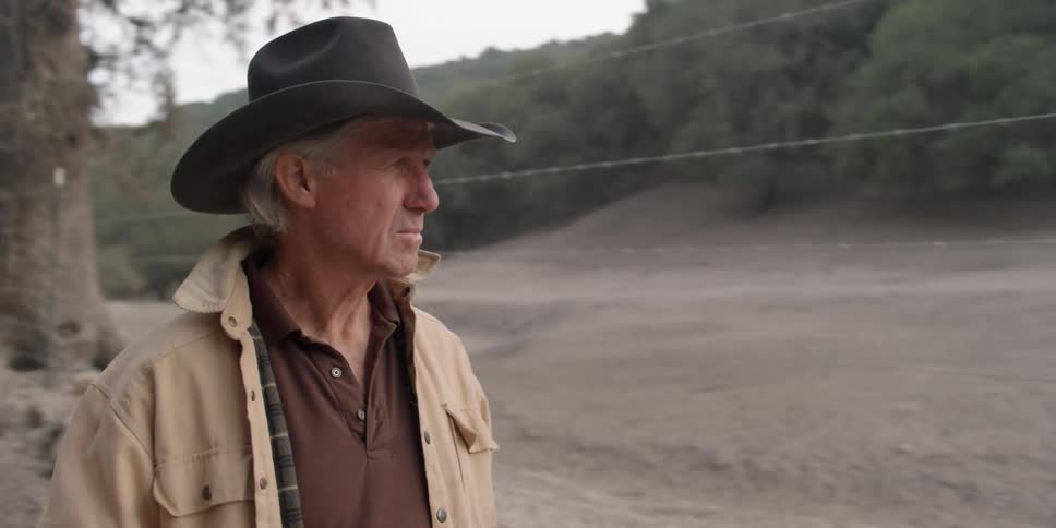 A cowboy walks next to a barbed wire fence on a ranch