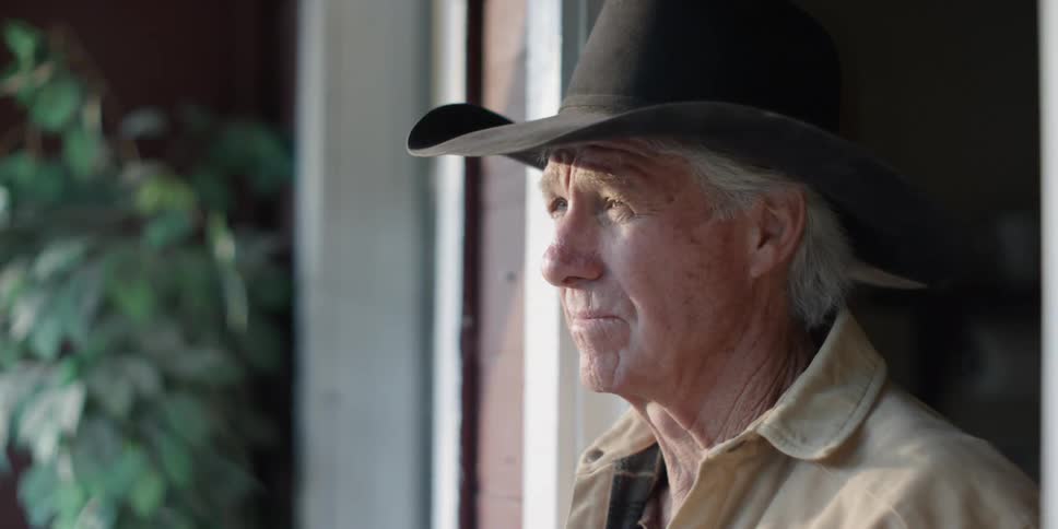 Elderly man wearing a cowboy hat looks on