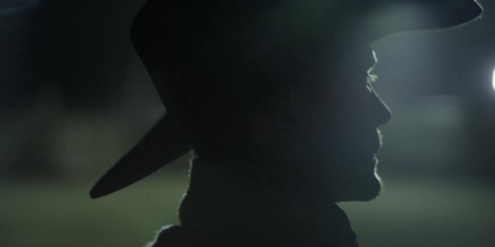 A light shines on a cowboy standing outside