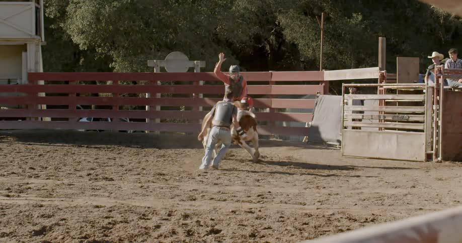A cowboy is performing in the rodeo riding a bull