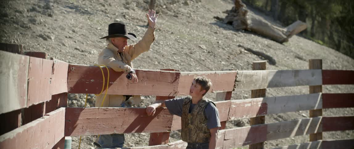 A cowboy leans over the wooden railing talking to someone inside
