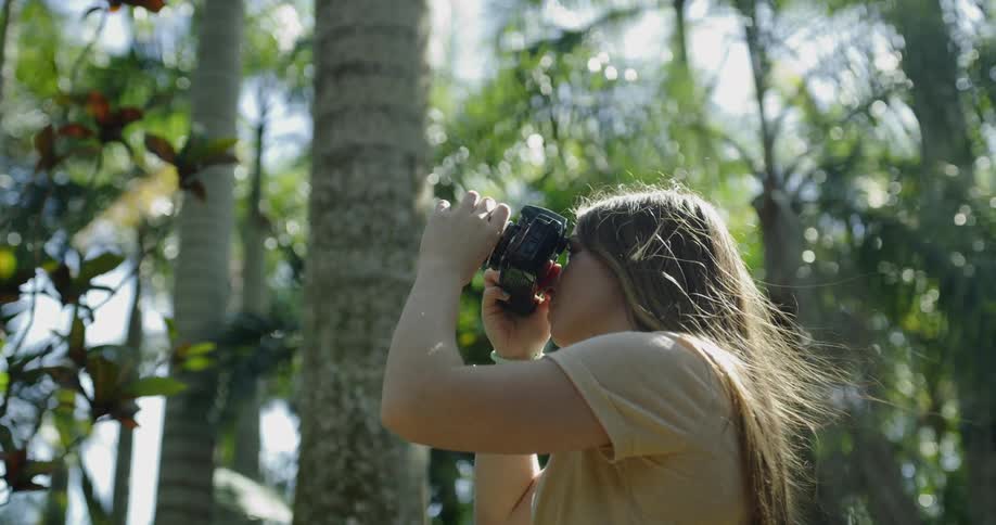 Woman standing by trees takes pictures on a sunny day