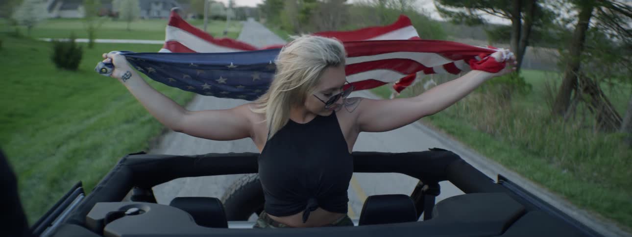 Woman rides on top of a vehicle holding a flag out