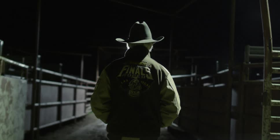 A cowboy walks in a paddock at night