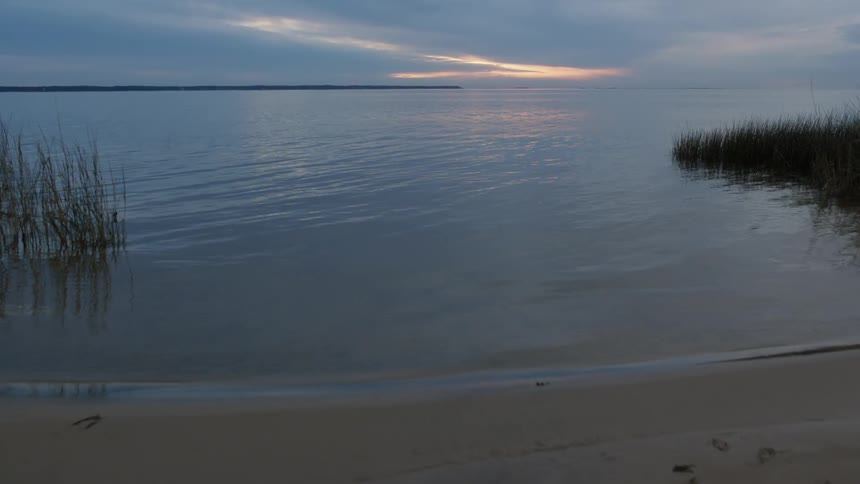 The water is calm near the shore at sunset