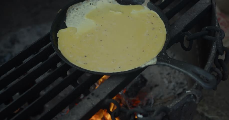 Eggs are cooking in a cast iron pan over a fire