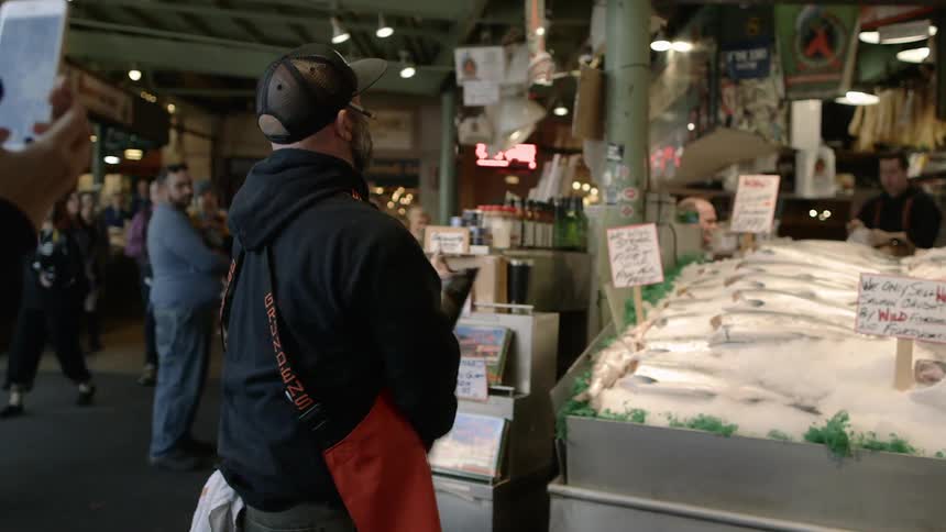 Men in a fish market toss a fish back and forth